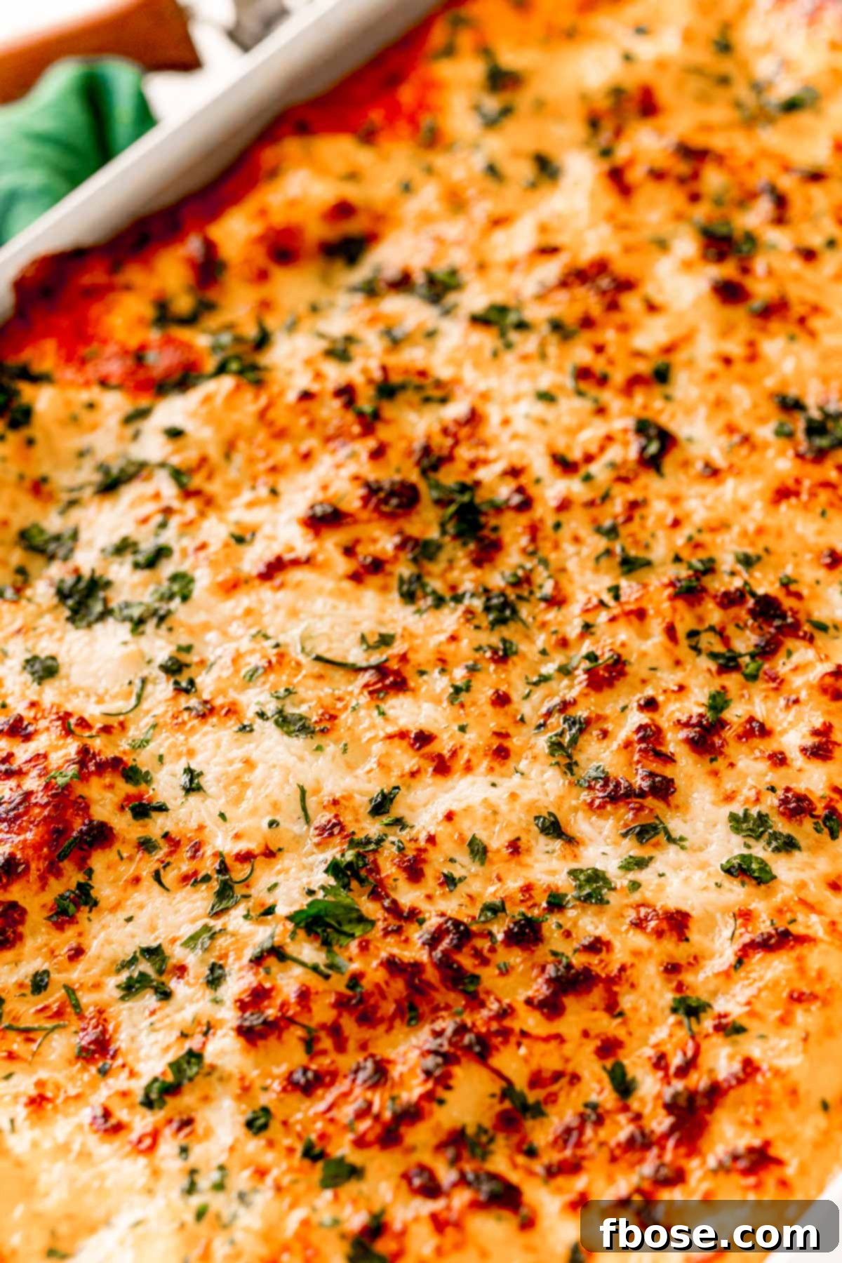 Angled photo of the top of a ravioli lasagna with bubbly, golden-brown cheese and rich sauce.
