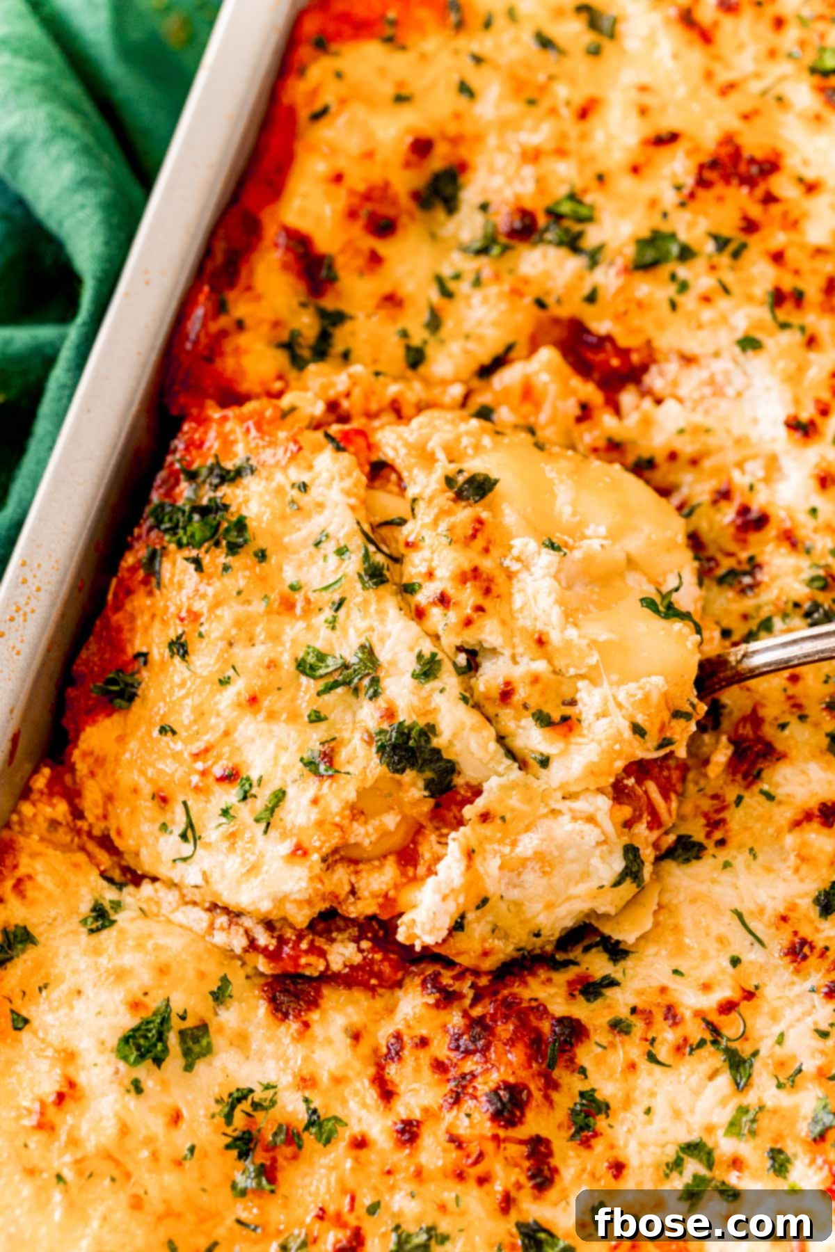 A spatula scooping a serving of ravioli lasagna out of a pan, revealing cheesy and saucy layers.
