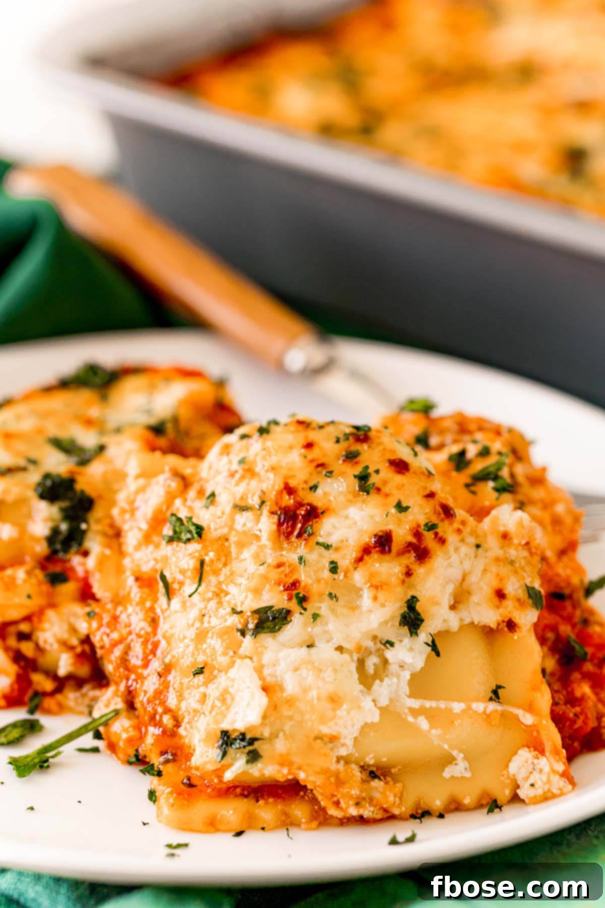 A serving of ravioli lasagna on a white plate, garnished with fresh parsley.