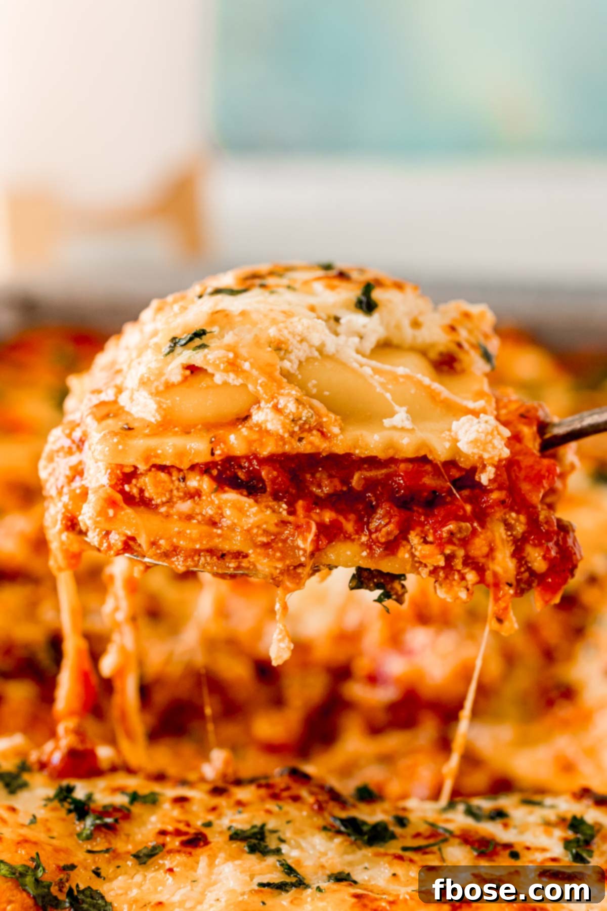 Ravioli lasagna being scooped out of a pan, showing a perfectly golden and bubbly top.