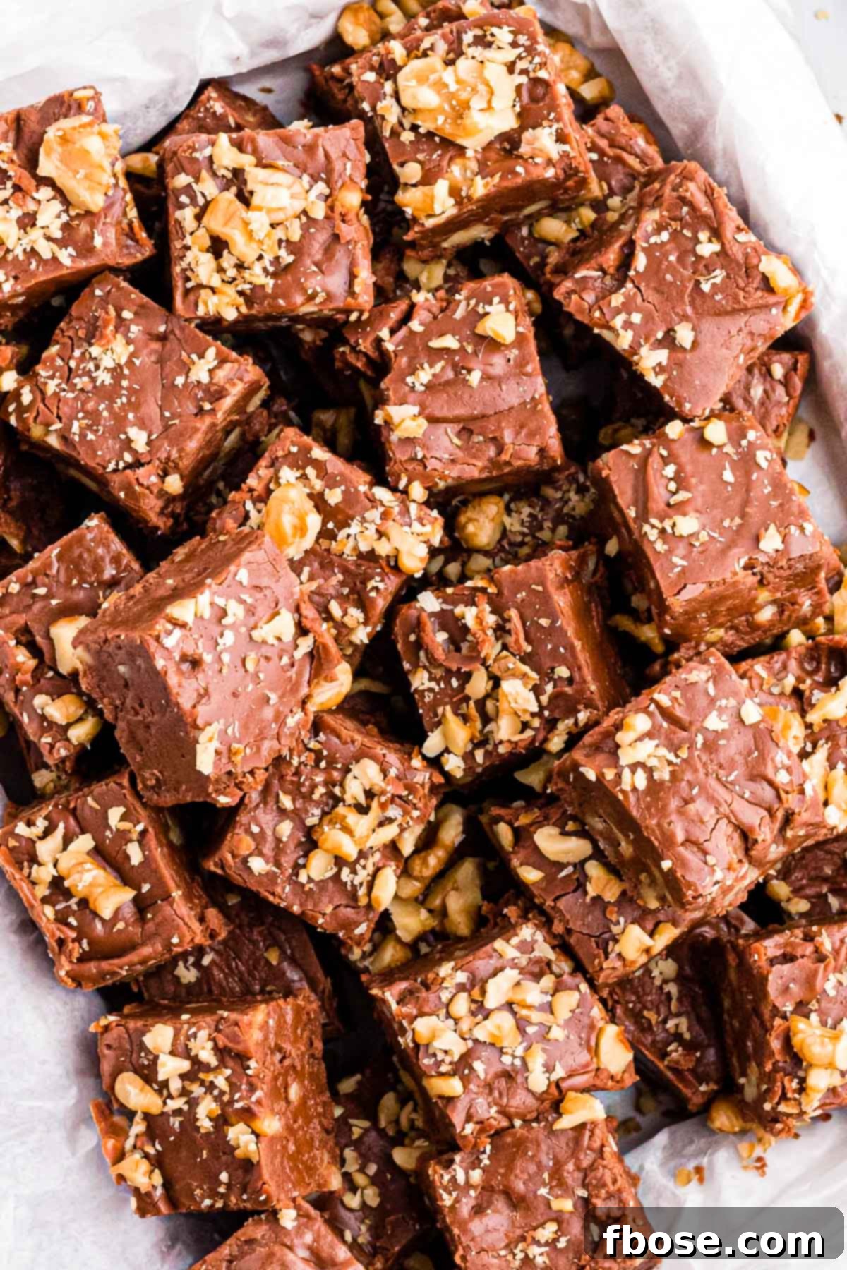 Overhead photo of a bunch of pieces of walnut chocolate fudge on a plate, highlighting its rich color and generous walnut topping.