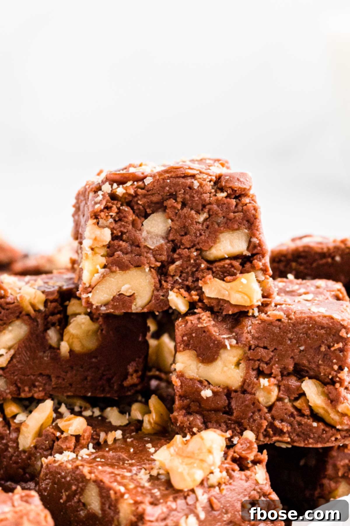 Close-up photo of several rich walnut chocolate fudge pieces stacked on top of each other, showing the embedded nuts.