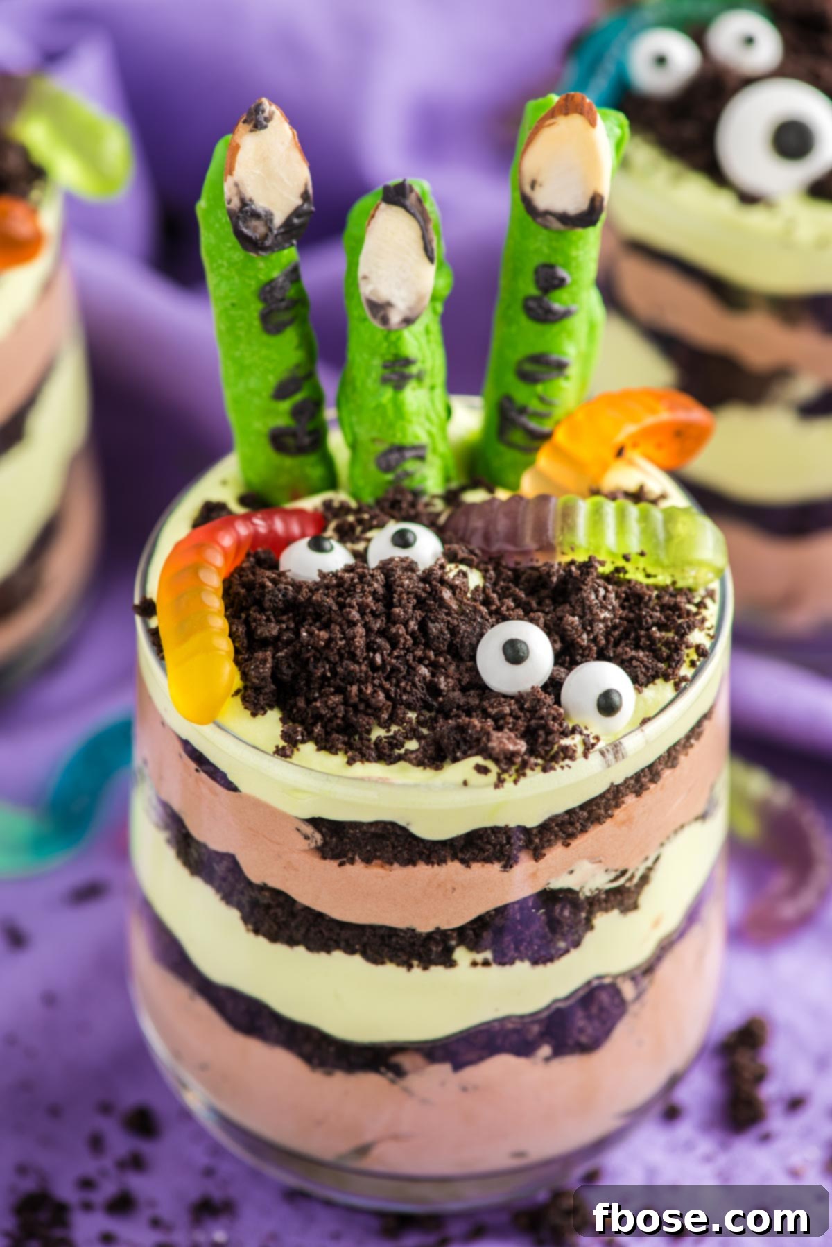 Close up photo of layers Halloween dirt cups with pretzel stick witch fingers, candy eyes, and gummy worms.