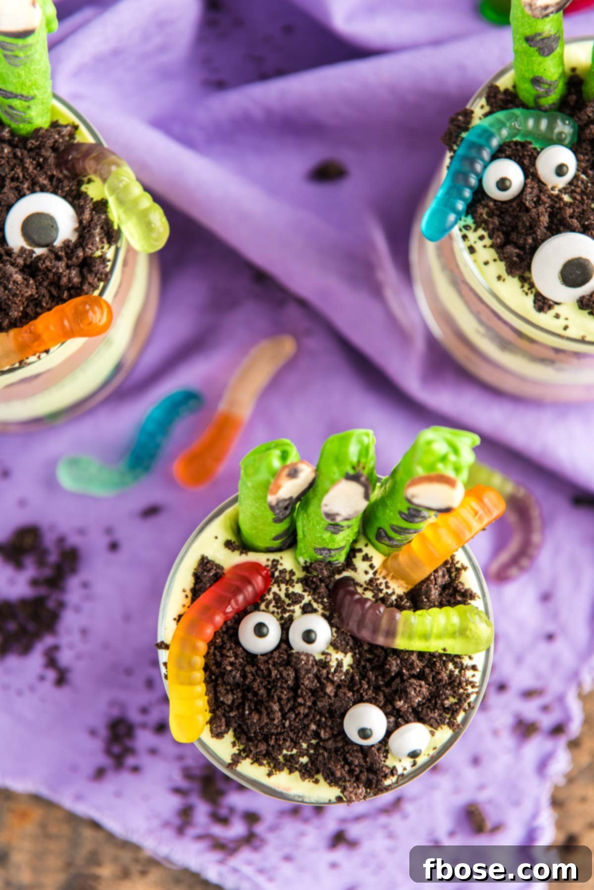 Close up photo of layers Halloween dirt cups with pretzel stick witch fingers, candy eyes, and gummy worms.