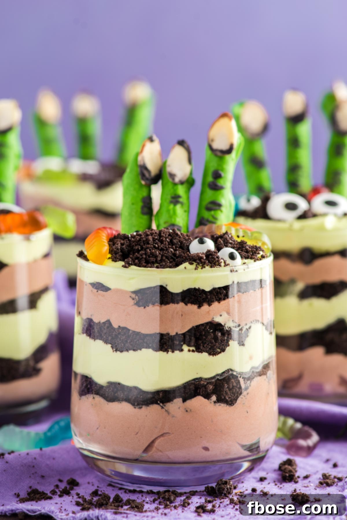 Close up photo of layers Halloween dirt cups with pretzel stick witch fingers, candy eyes, and gummy worms.