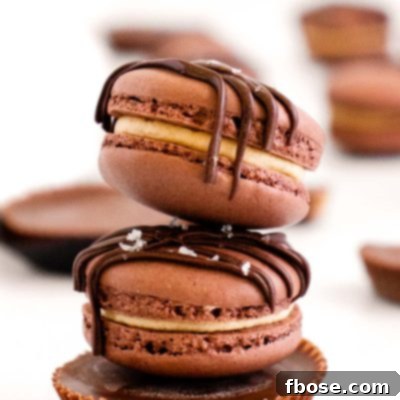 Two peanut butter chocolate macarons stacked on top of a peanut butter cup on a white table.