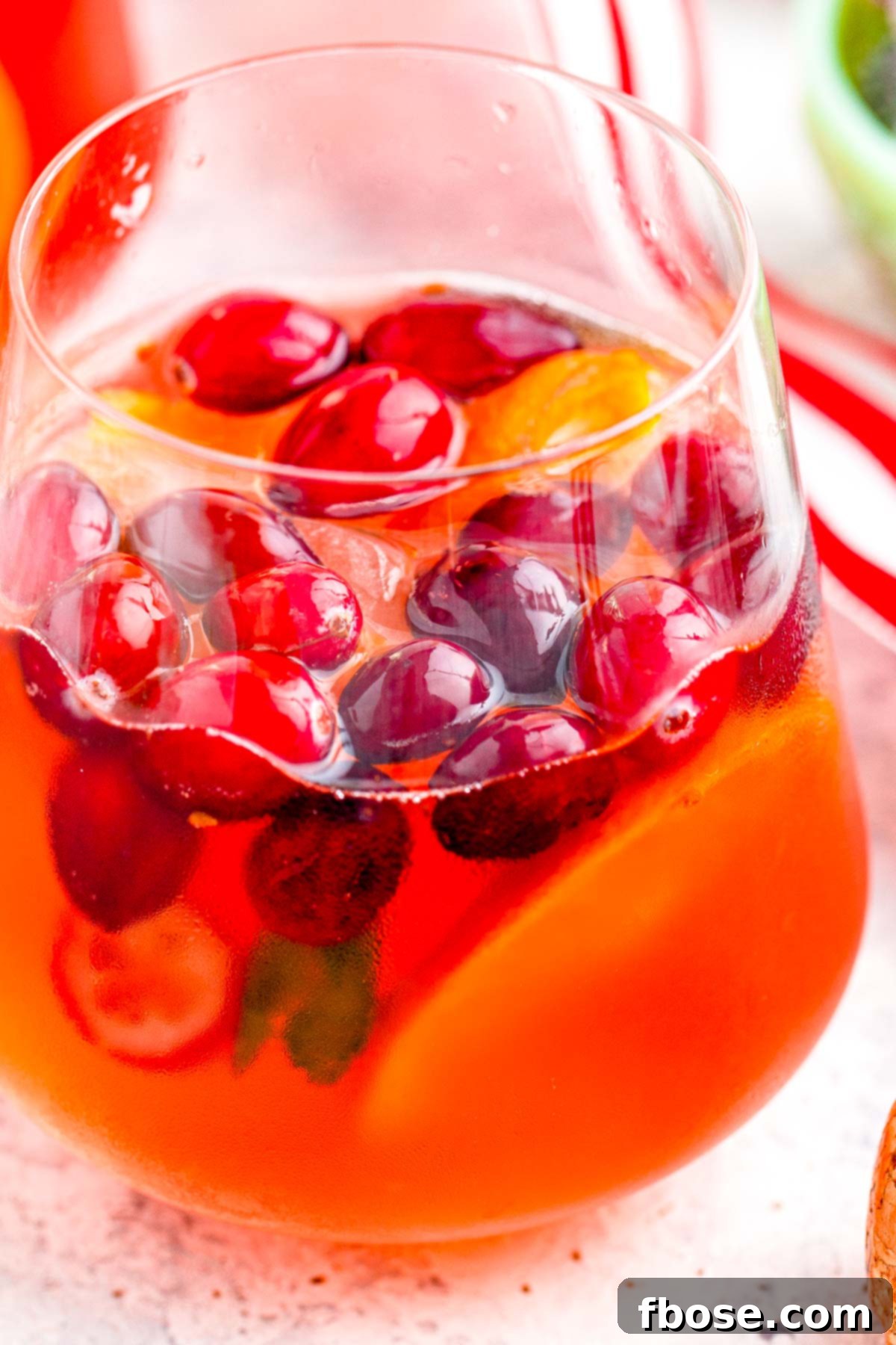 Crimson & Citrus Yuletide Sparkler 3 A close-up shot of a glass filled with sparkling Christmas Mimosa Punch, adorned with a fresh cranberry and a small sprig of rosemary, against a soft, festive background.