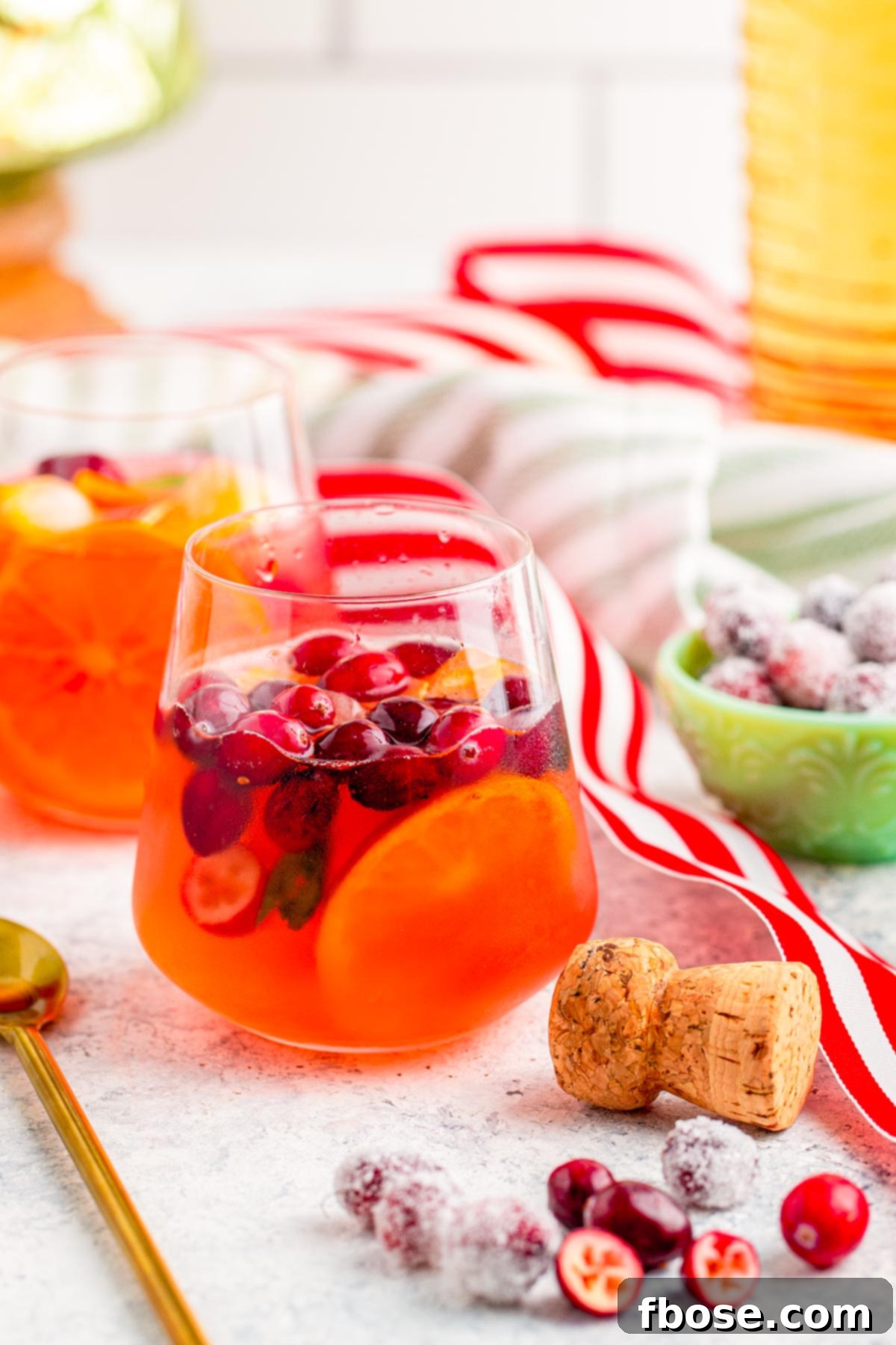 Crimson & Citrus Yuletide Sparkler 9 A single glass of Christmas Mimosa Punch, garnished with fresh cranberries and an orange slice, sitting on a wooden table with scattered holiday decorations like pinecones and fairy lights, creating a warm and inviting festive scene.