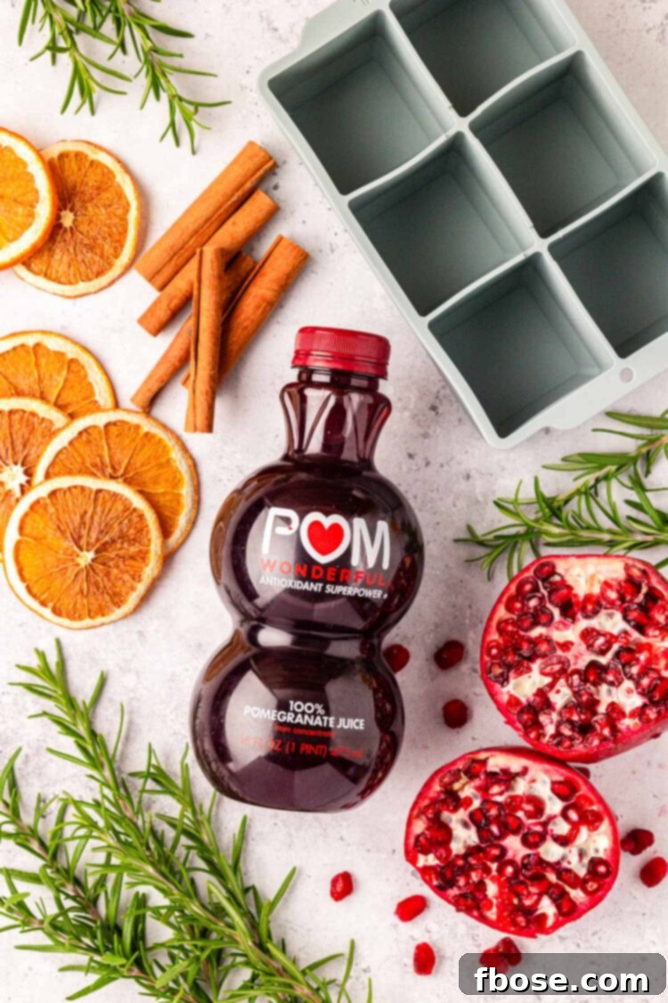 Overhead photo of a bottle of pomegranate juice and various garnishes near an ice cube tray, ready for making decorative ice cubes.