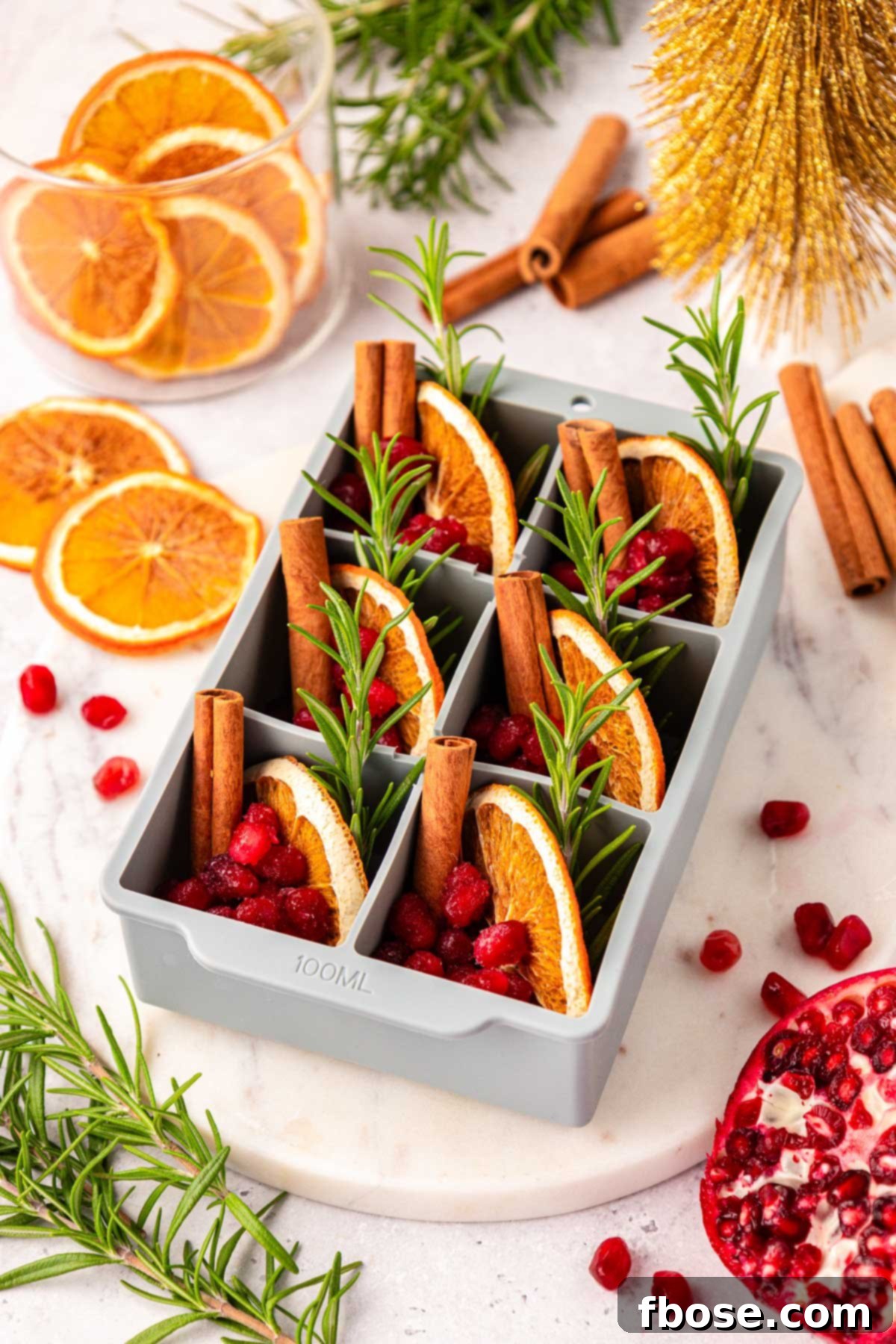 Garnished ice cube trays filled with fruit, mint, and water, ready to be frozen for holiday drinks.
