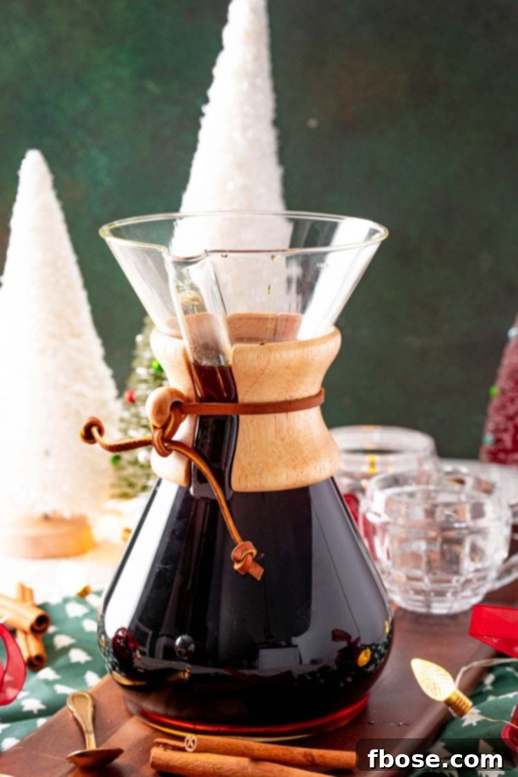 A glass carafe filled with freshly brewed Christmas spiced coffee, adorned with festive holiday decorations on a wooden table.