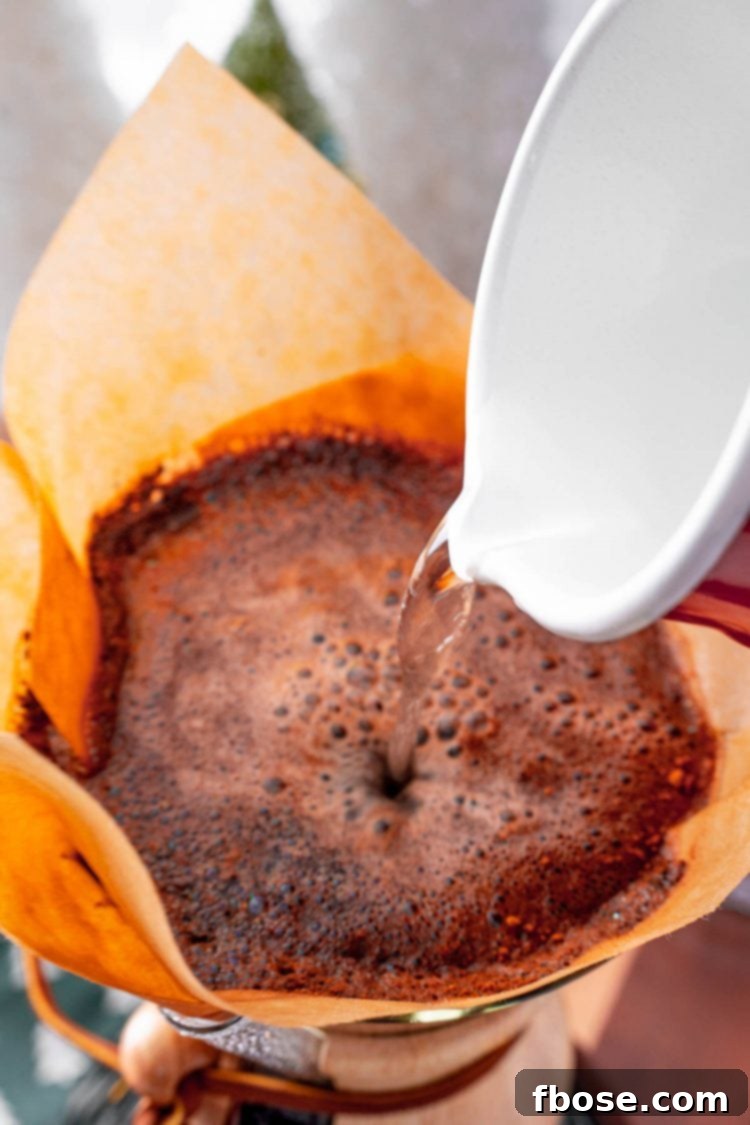 Hot water being poured over the spiced coffee grounds in a pour-over carafe, highlighting the brewing process.
