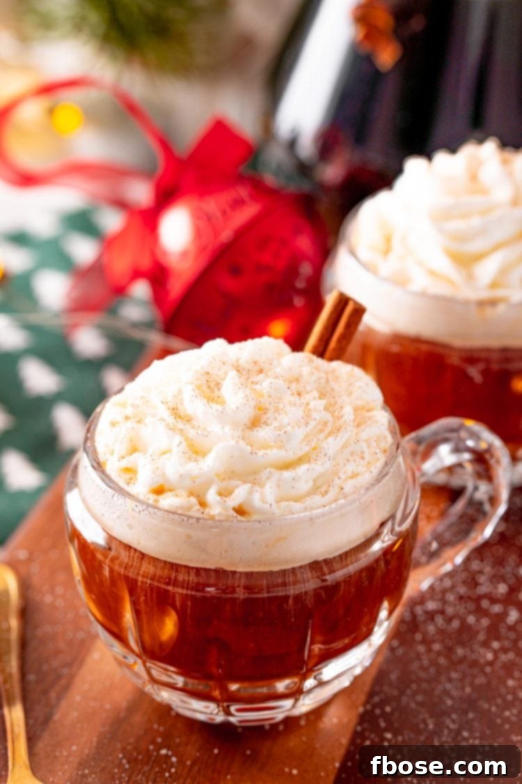 Close-up photo of coffee in a small rounded mug topped with whipped cream, sprinkled with cinnamon, and garnished with a cinnamon stick, evoking holiday warmth.