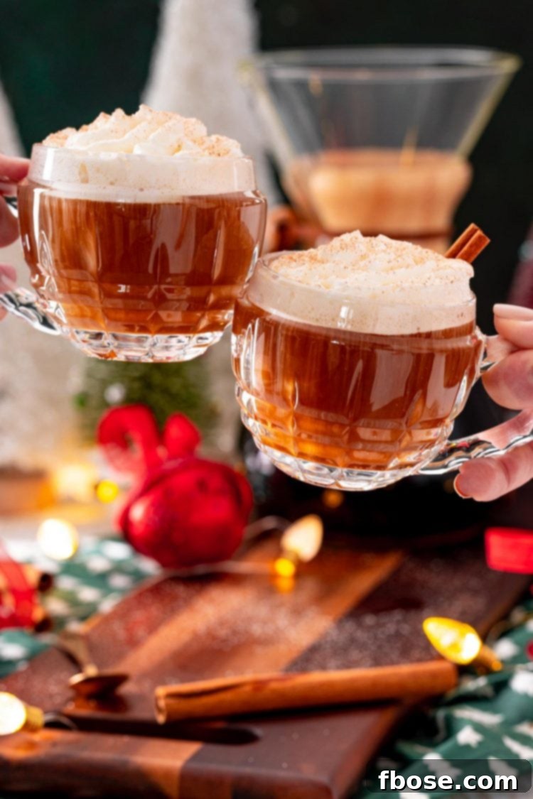 Two mugs of Christmas spiced coffee being clinked together over a table adorned with various holiday decorations, signifying celebration.