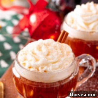 Close up photo of coffee in a small rounded mug topped with whipped cream and cinnamon and garnished with a cinnamon stick.