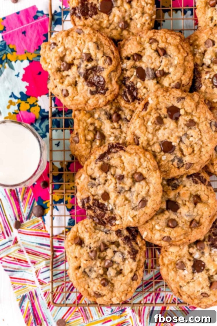 Overhead photo of ranger cookies on a wire rack on a colorful napkin with a glass of milk next to it.