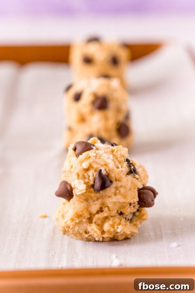 Close up photo of balls of cookie dough on a parchment lined baking sheet.