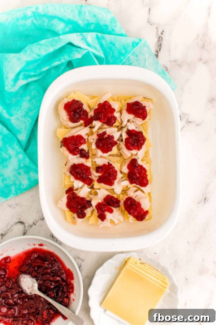 Overhead photo of thanksgiving sliders being prepared in a white casserole dish on a marble counter.