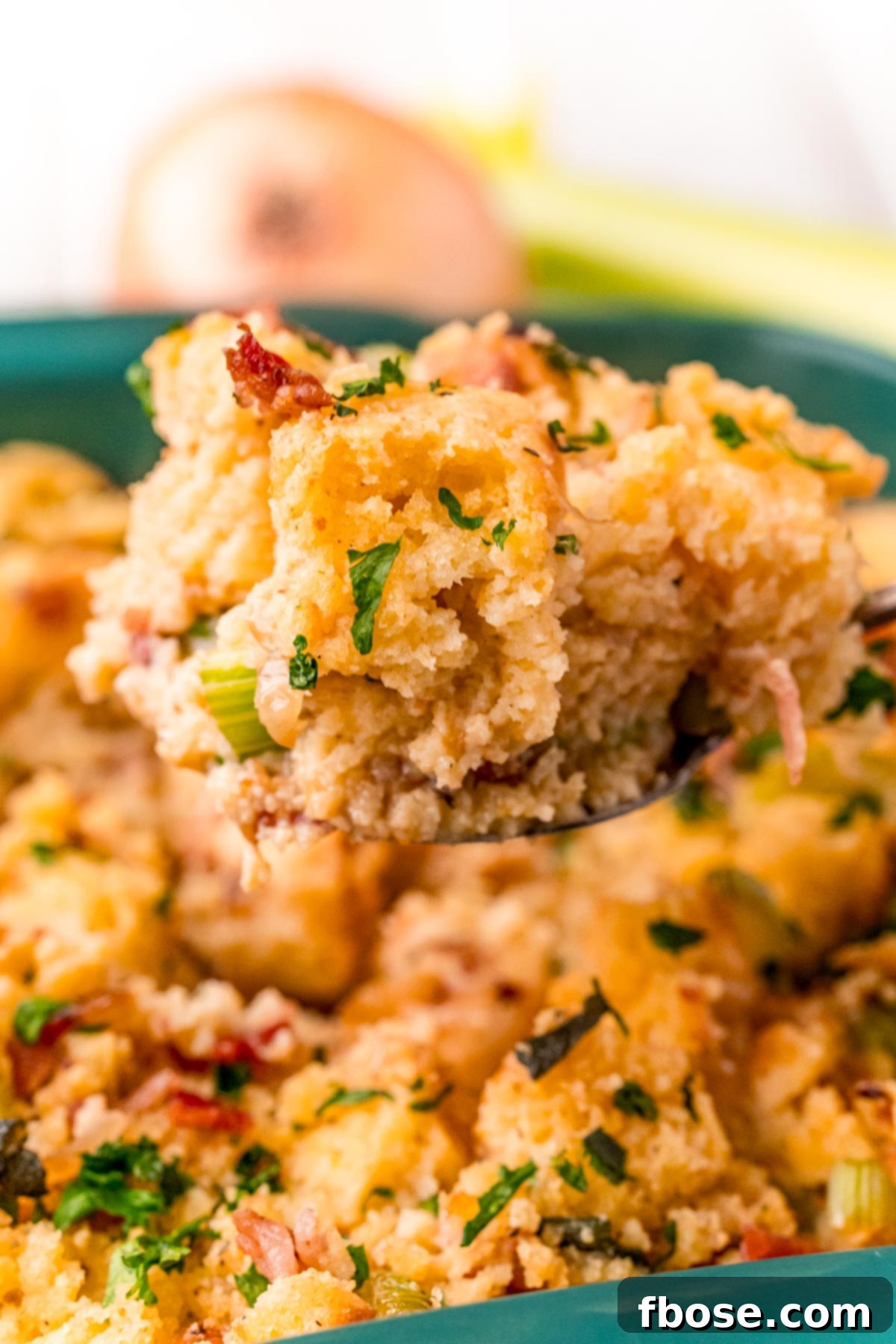 The Ultimate Cornbread Dressing 8 A serving spoon lifting a generous scoop of Southern Cornbread Dressing from a teal baking dish, showing its delicious texture.