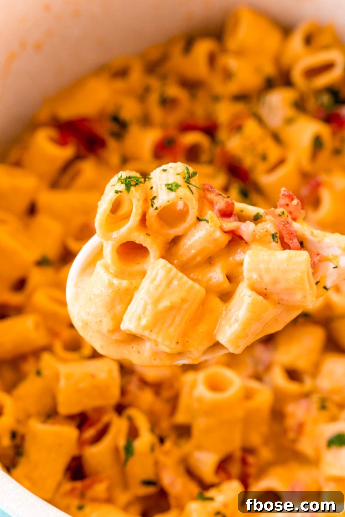 A white serving spoon lifting a scoop of mac and cheese with bacon out of a pot.