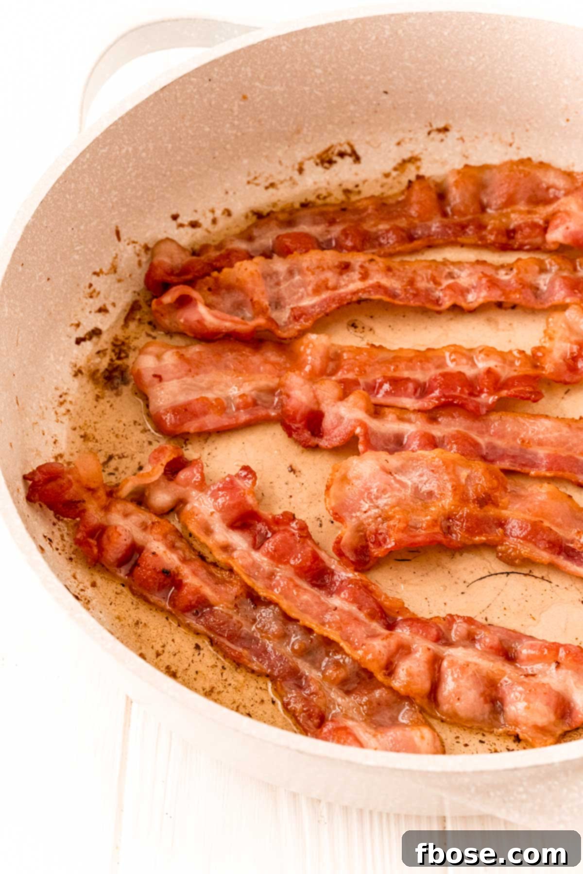 Bacon cooking in a tan skillet.