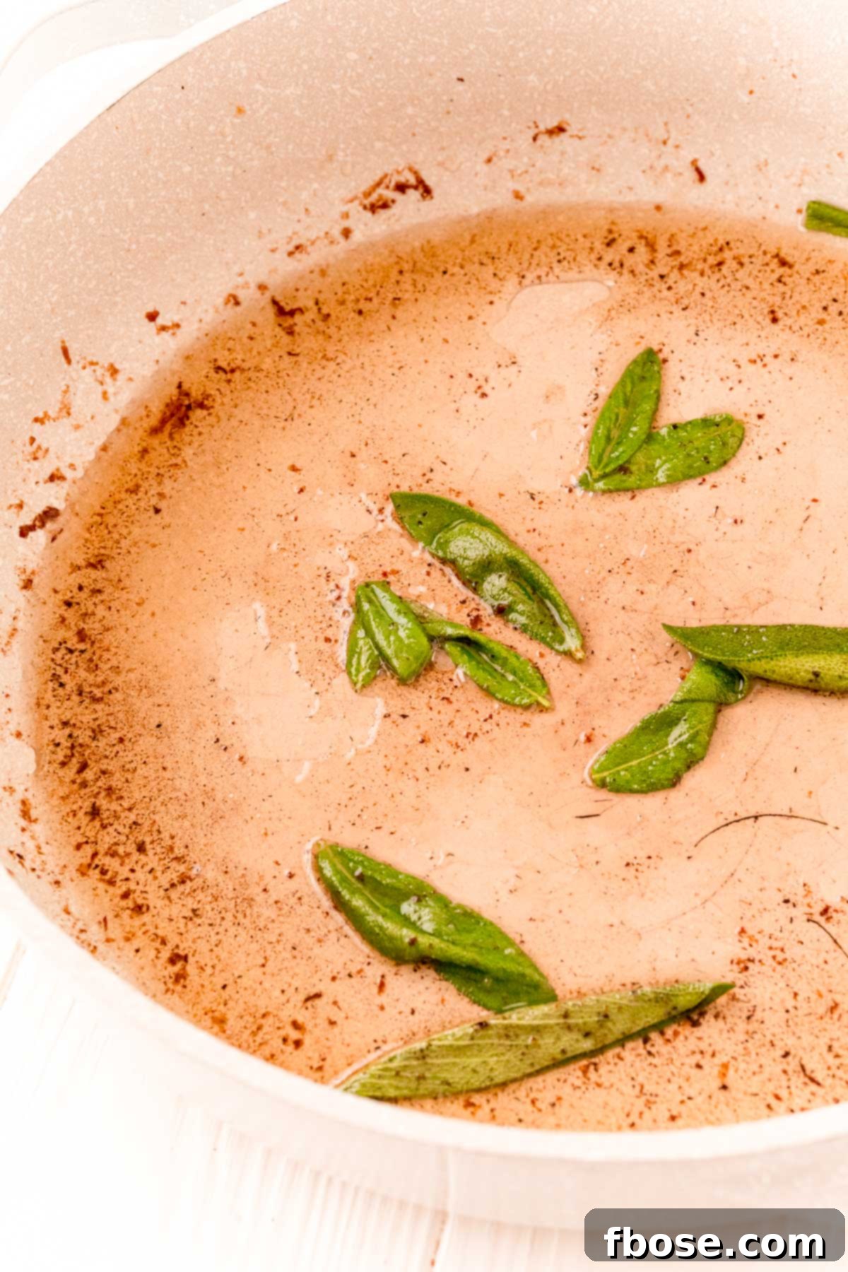 Sage being cooked in a tan frying pan.