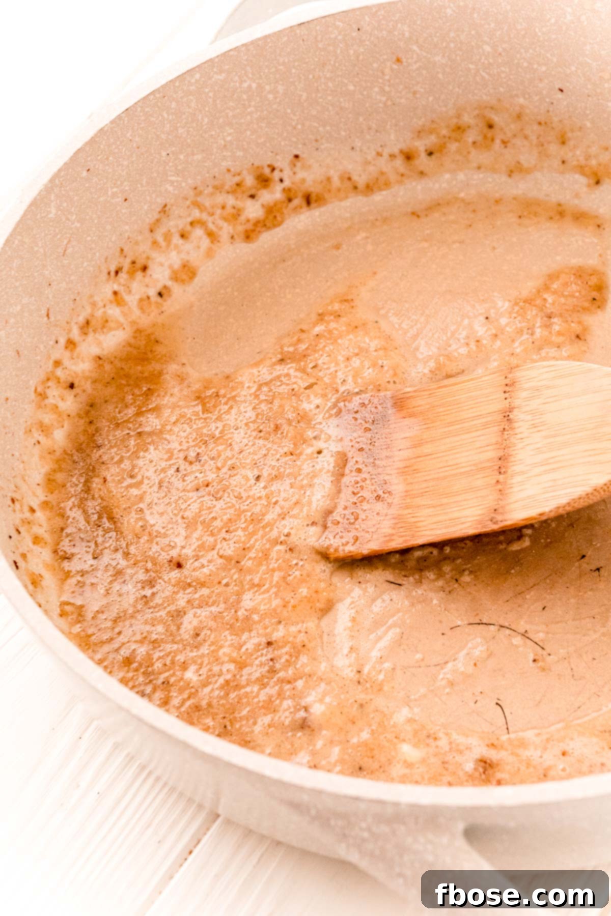 Garlic and flour being cooked in a tan skillet.