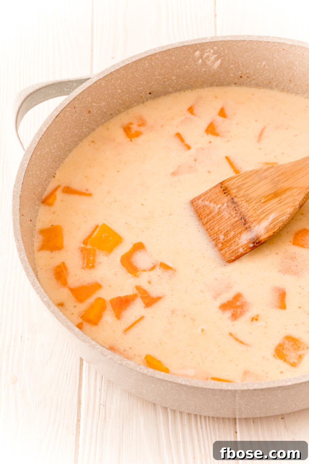 butternut squash cubes, broth, milk, and cream with spices cooking in a tan skillet.