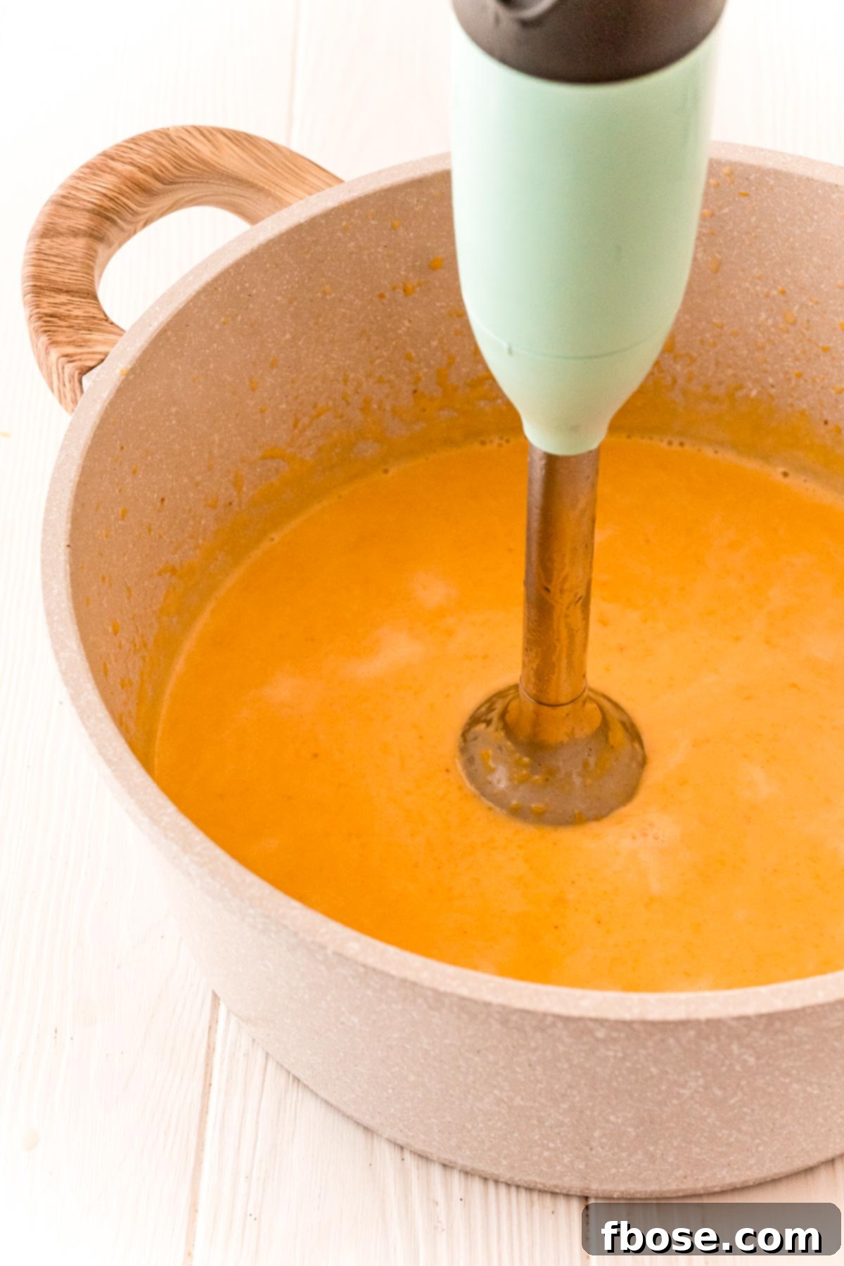 An immersion blender blending butternut cream sauce.
