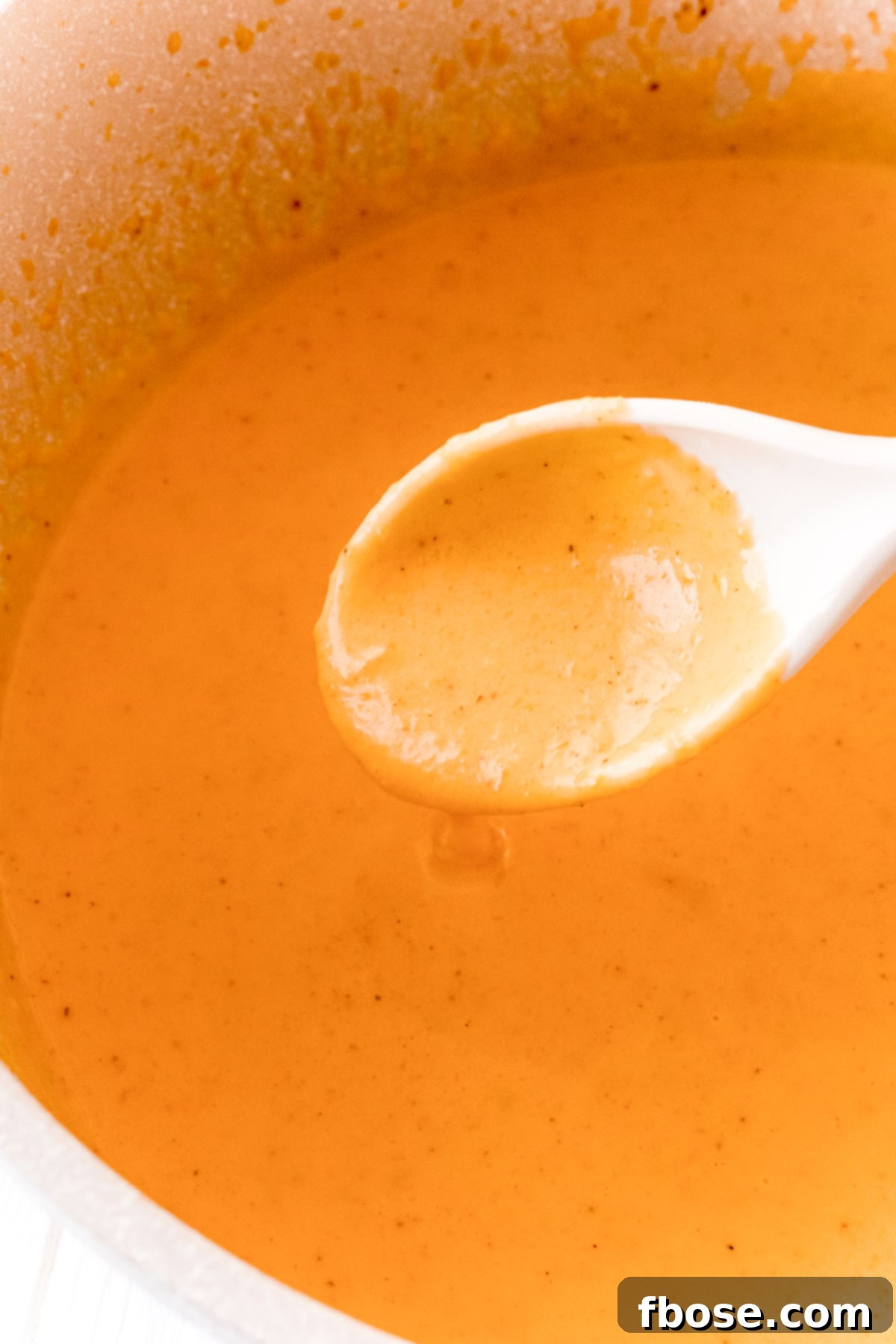 Butternut cream sauce in a pan being scooped up with a white spoon.