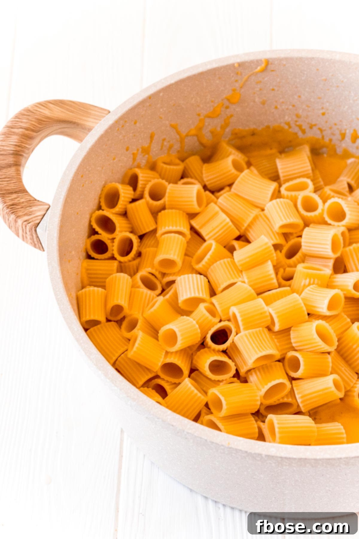 Pasta being added to a pot filled with butternut cream sauce.