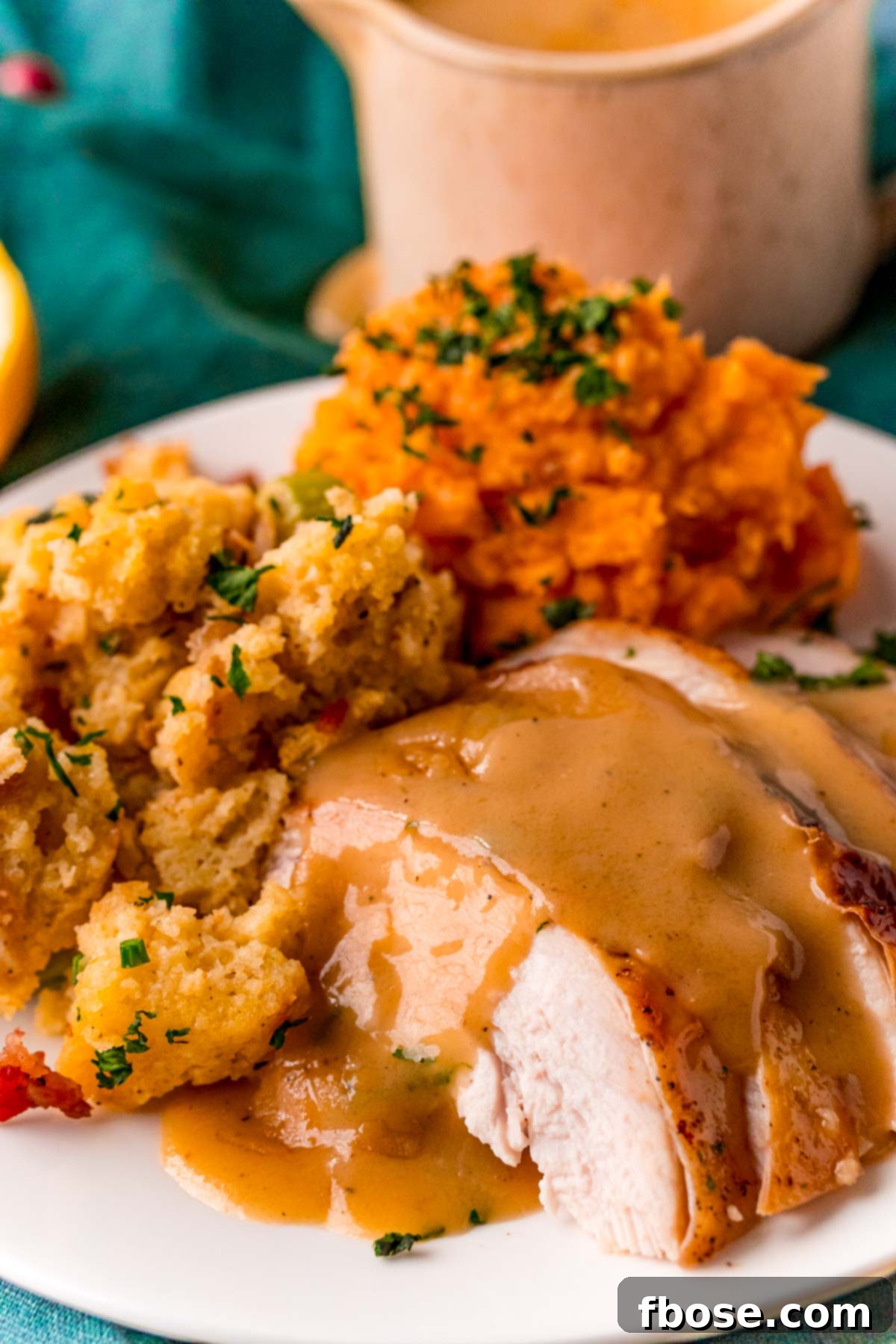 Beautifully sliced turkey breast topped with rich gravy, accompanied by savory stuffing and creamy sweet potatoes on a plate.