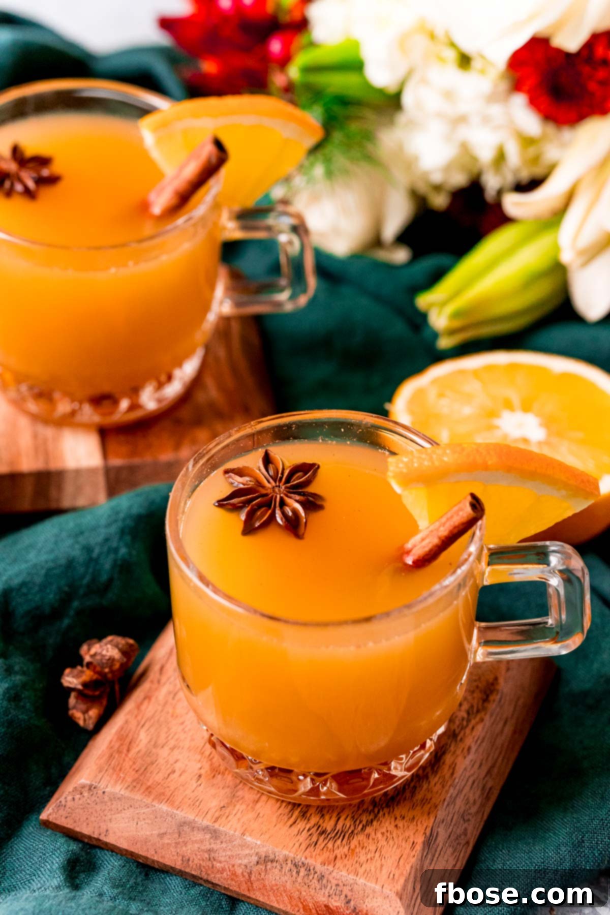 Two glass mugs of wassail on wooden coasters on a green napkin.