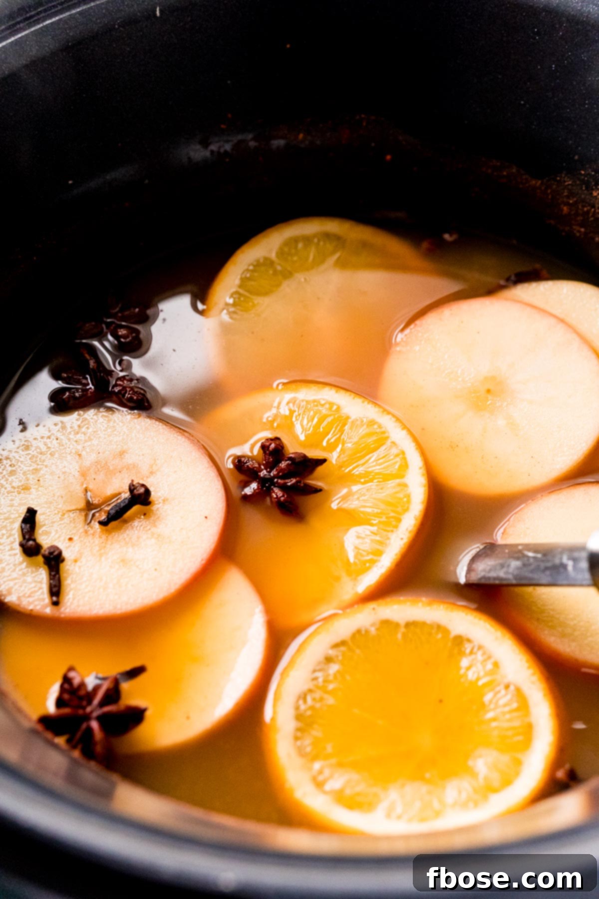 Wassail in a crockpot with sliced oranges and apples and star anise and cloves.