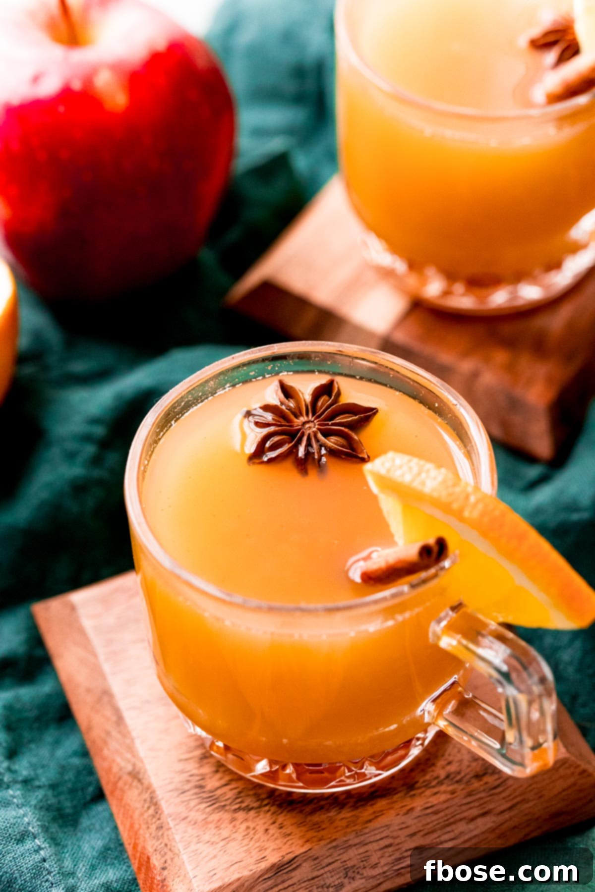 Close up photo of wassail in glass mugs garnished with cinnamon sticks and star anise.
