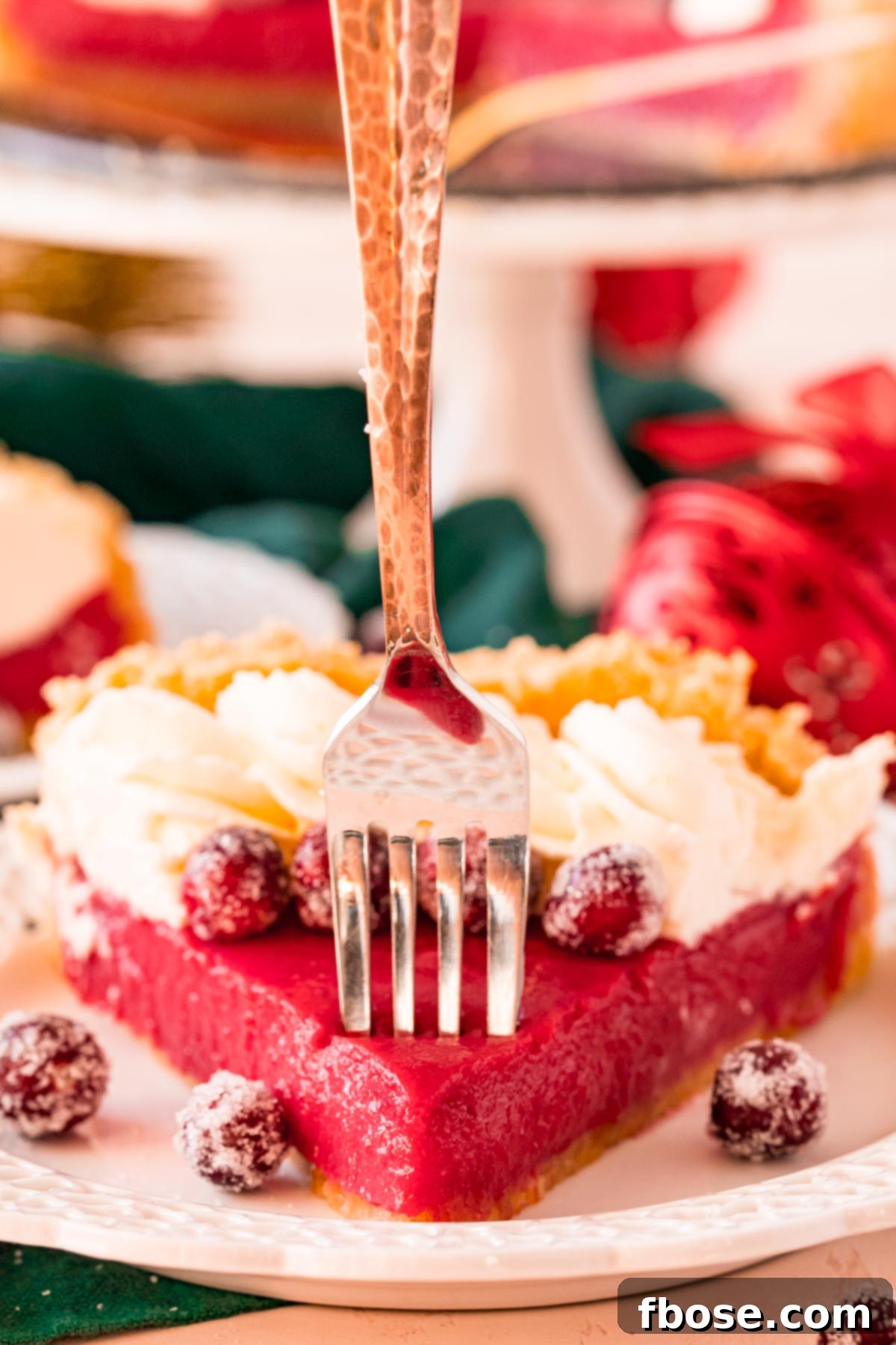 A fork gently taking a bite out of a creamy cranberry pie slice, revealing the smooth filling and shortbread crust.