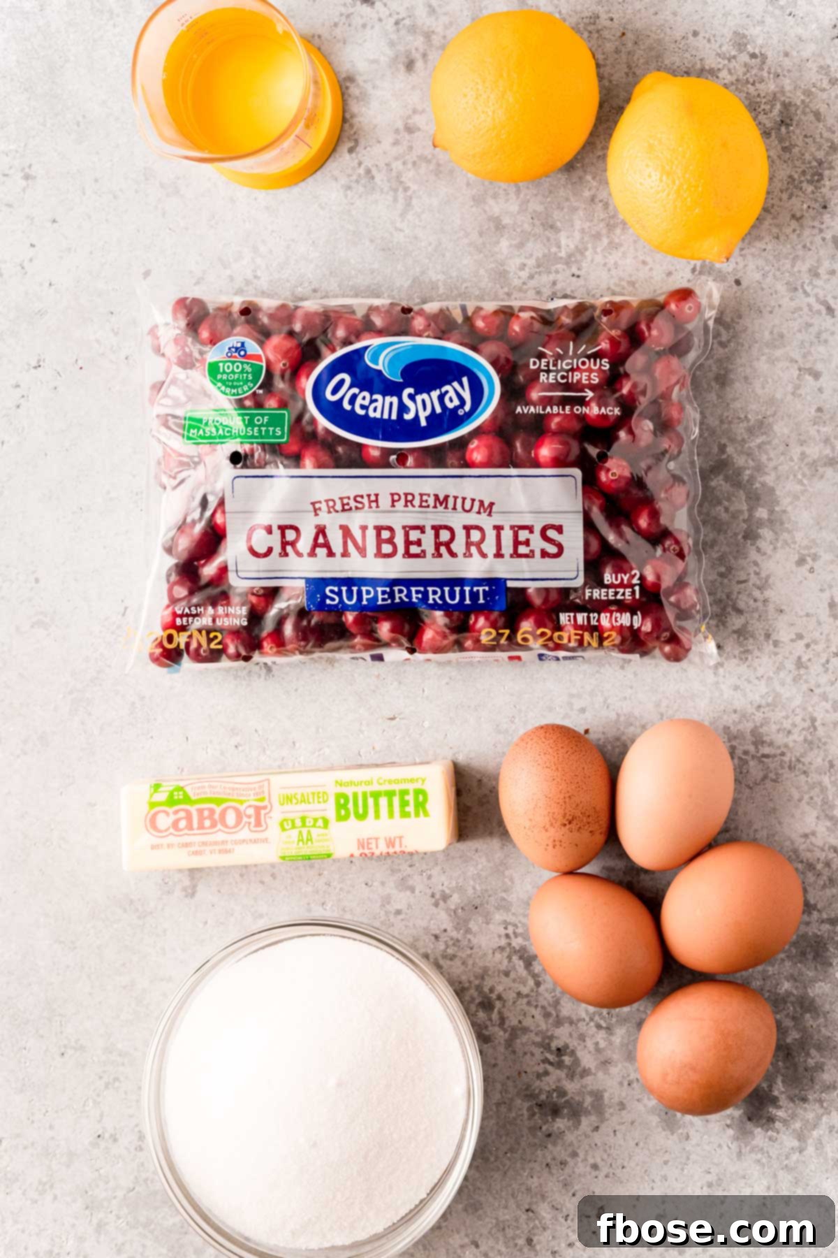 Overhead photo of ingredients to make the filling for cranberry pie, including fresh cranberries, sugar, butter, and eggs, arranged neatly on a surface.