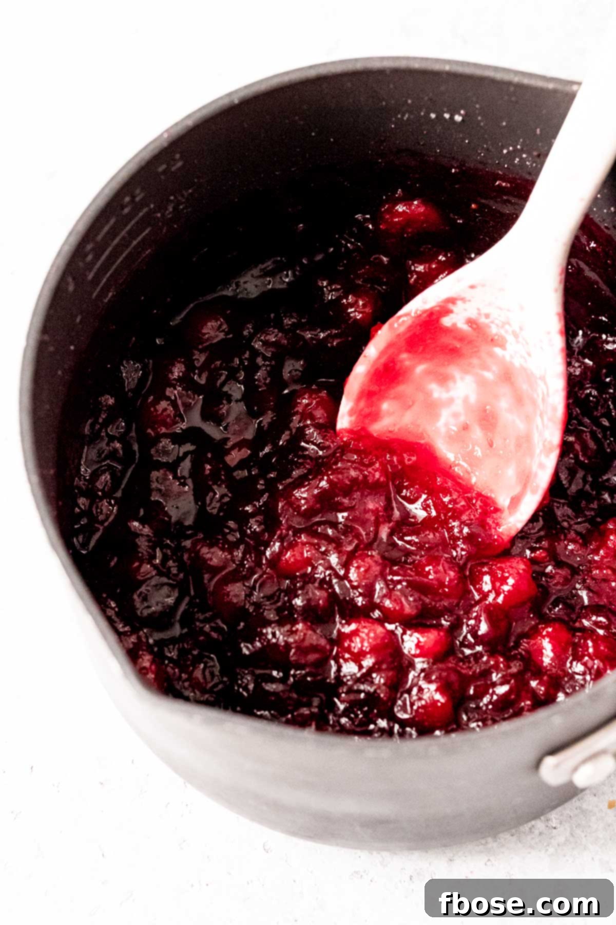 Fresh cranberries being cooked in a medium saucepan on a stovetop, with steam gently rising.