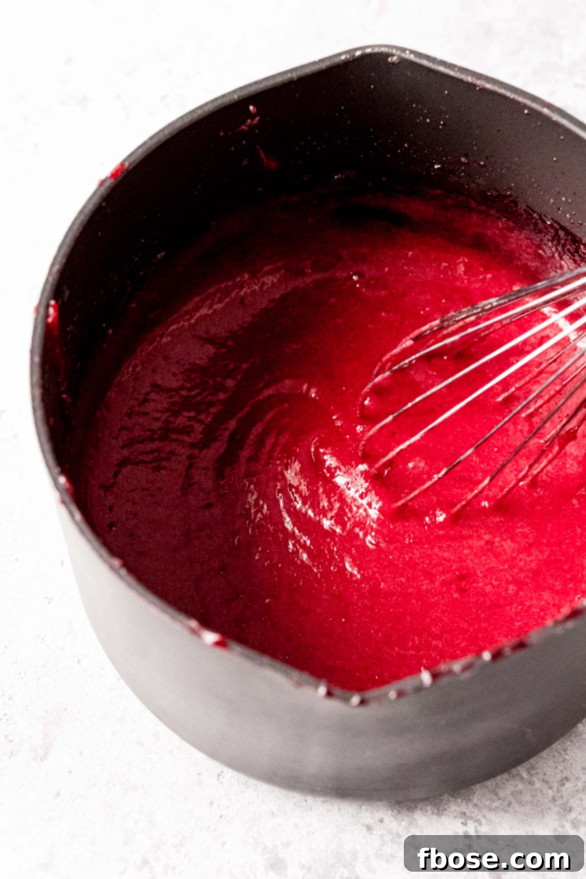 Smooth, thickened cranberry curd in a medium saucepan, with a whisk resting in it after stirring in butter and lemon juice.