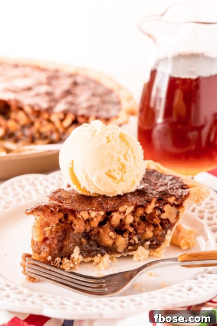 A perfectly sliced Maple Walnut Pie on a white plate, served with a fork, with the remaining pie and a pitcher of maple syrup in the soft-focus background.