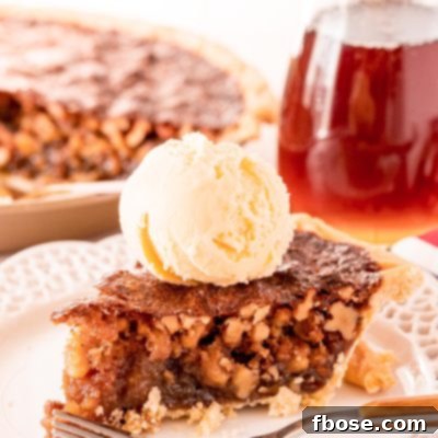 A slice of Maple Walnut Pie on a white plate with a fork. Pitcher of maple syrup and the rest of the pie are in the background.