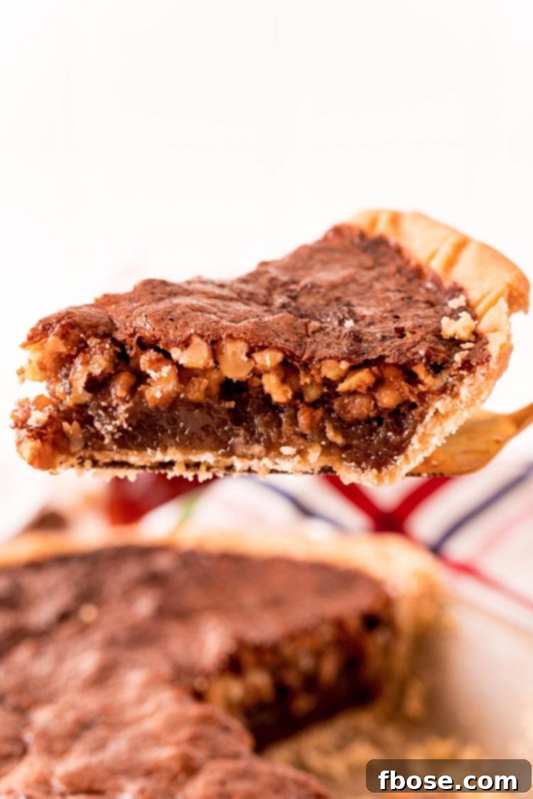 A slice of Maple Walnut Pie being carefully lifted from the whole pie in its pan with a silver pie server, showcasing its rich, gooey filling.