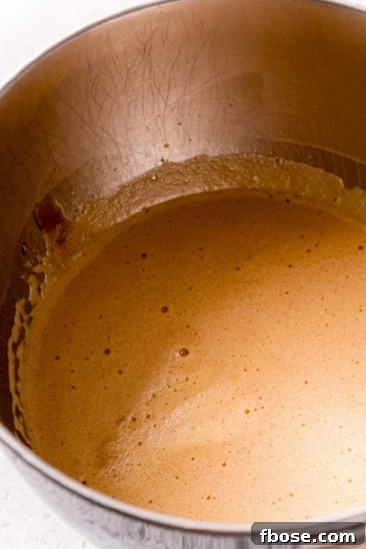 A rich, golden-brown walnut pie filling being mixed smoothly in a shiny stainless steel mixing bowl, ready for the nuts.