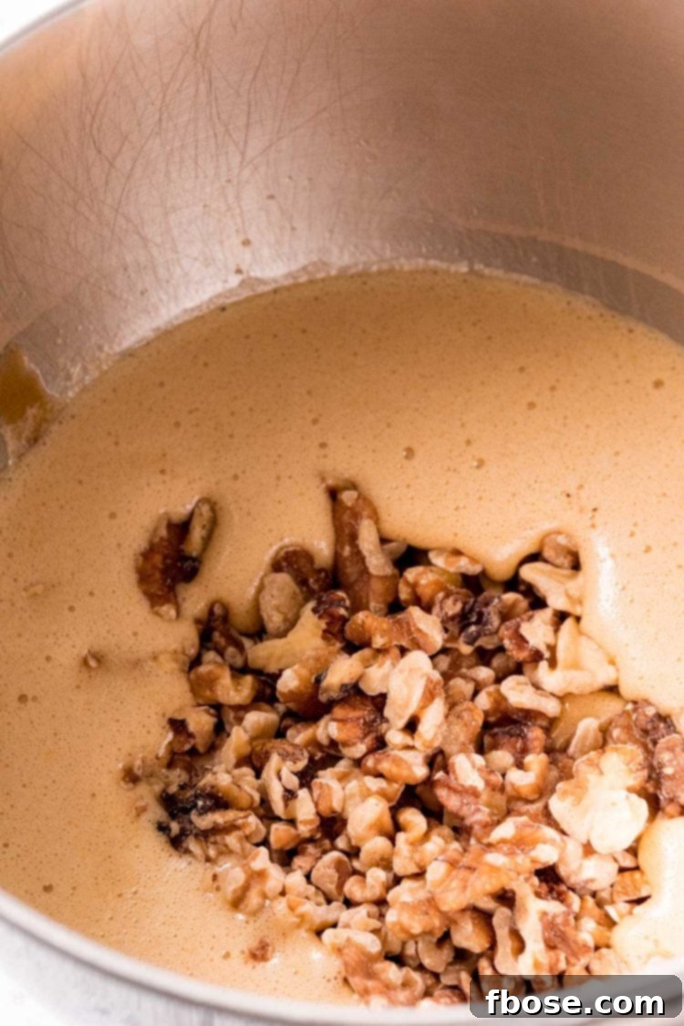 Chopped walnuts being gently folded into a rich pie filling in a mixing bowl with a spatula, ensuring even distribution.