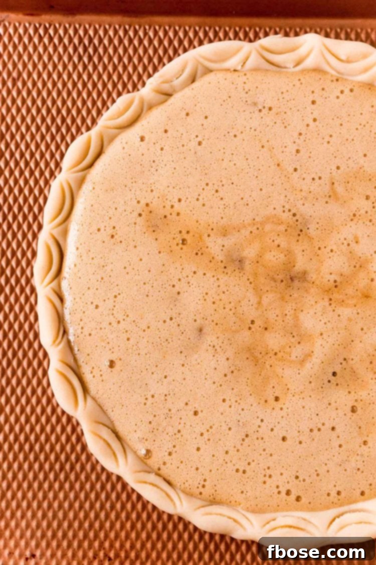 An unbaked Maple Walnut Pie sitting on a bronze cookie sheet, ready to be placed in the oven, with its perfectly fluted crust.