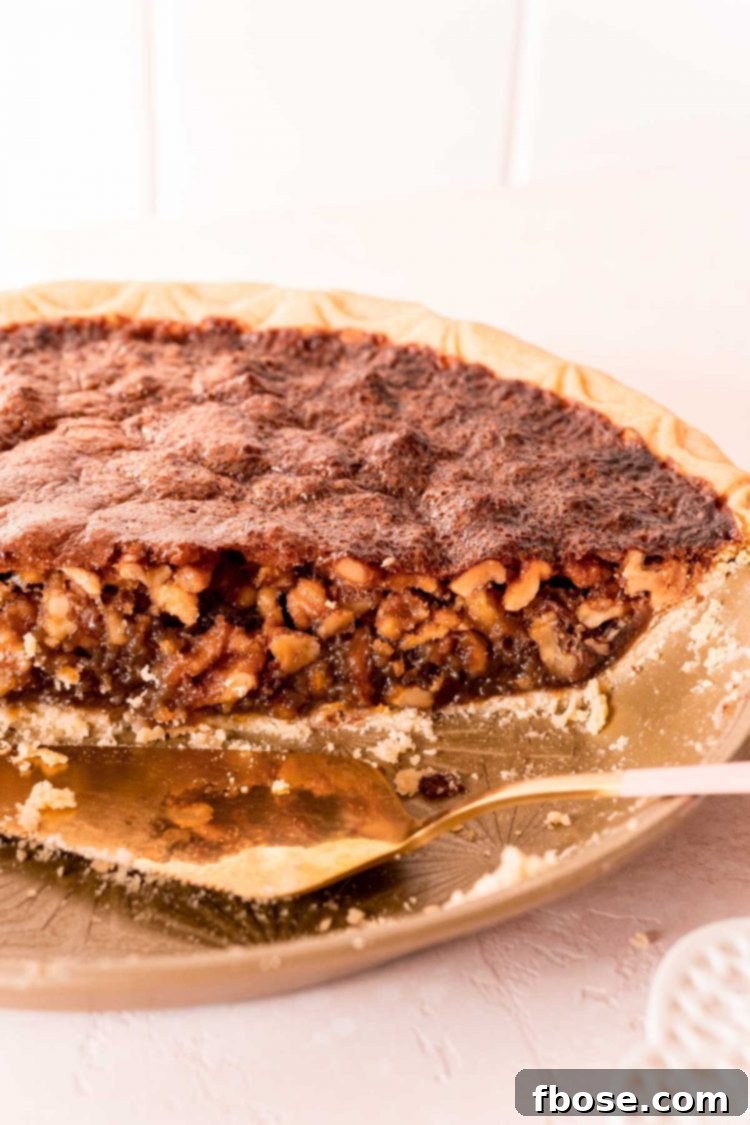 A beautiful half of a Maple Walnut Pie still resting in its pie pan, with a pie server poised nearby, inviting a second slice.