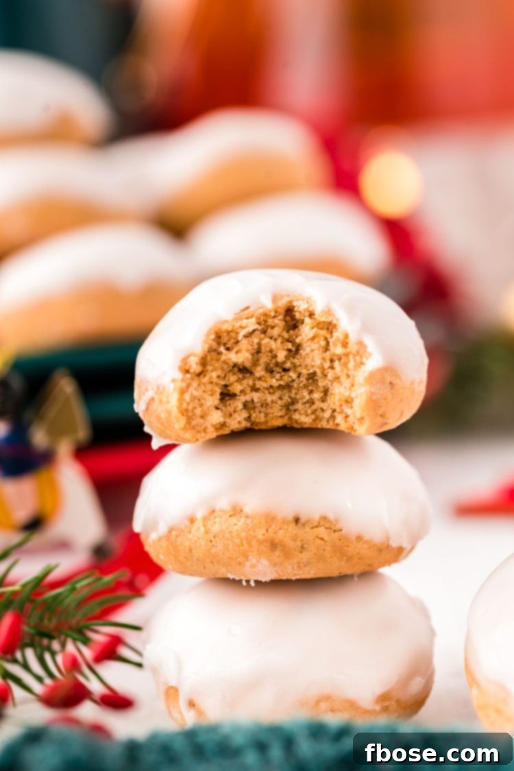 Close up photo of three pfeffernusse cookies stacked on op of each other with holiday decorations in the background.
