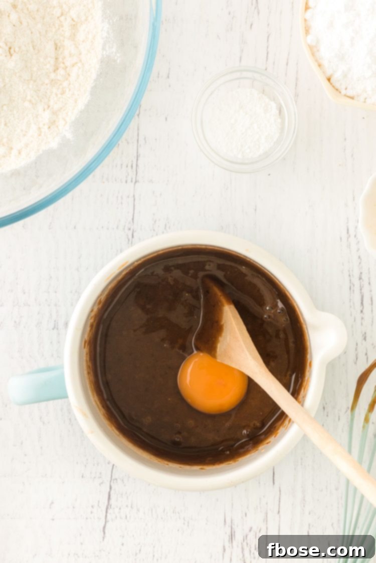 Egg being added into a pot with honey and brown sugar that has been melted.
