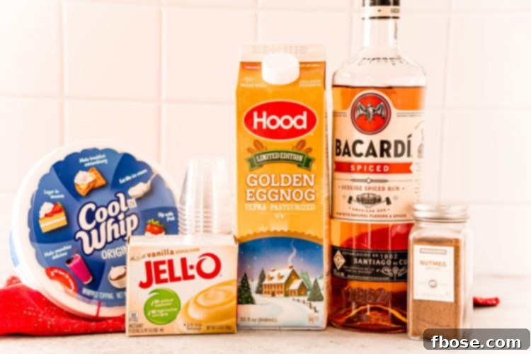 Ingredients for eggnog pudding shots, including eggnog, instant pudding mix, spiced rum, and whipped topping, arranged on a white table.