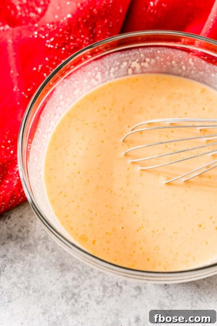 Vanilla pudding mix, eggnog, and rum being whisked together in a glass mixing bowl.